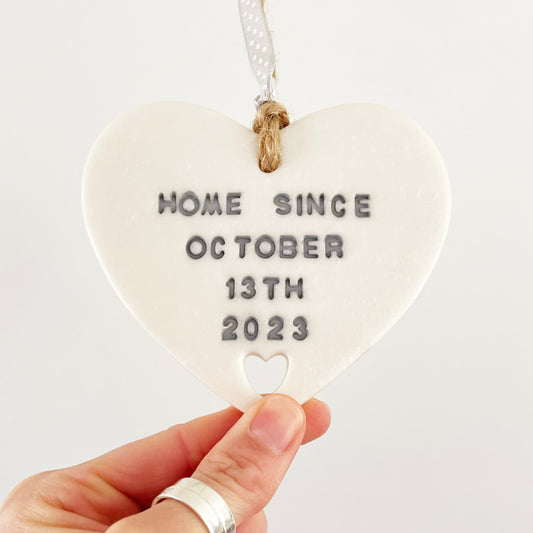 Personalised housewarming new home gift, pearlised white clay heart with a heart cut out at the bottom with jute twine for hanging, the heart is personalised in grey with HOME SINCE OCTOBER 13TH 2023