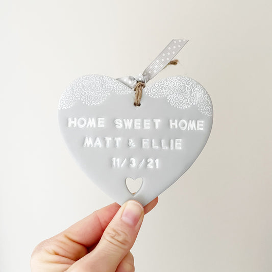 Personalised housewarming new home gift, grey clay heart with a white lace edge at the top of the heart and a heart cut out at the bottom with jute twine for hanging, the heart is personalised with HOME SWEET HOME MATT & ELLIE 11/3/21