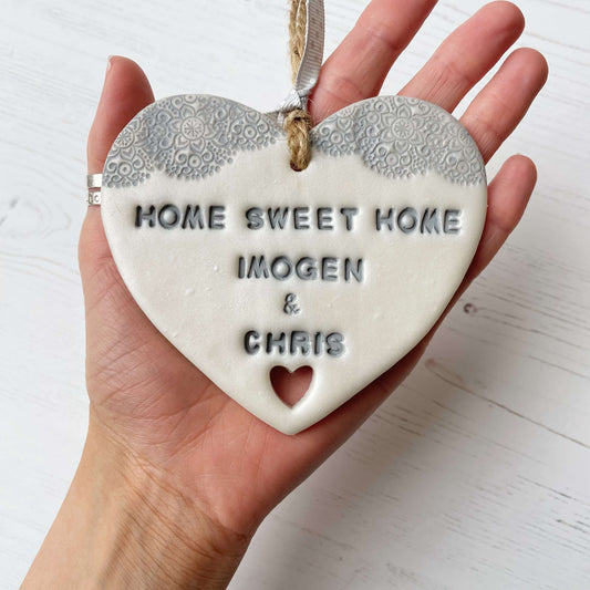 Personalised new home gift pearlised white clay heart with a grey lace edge at the top & a heart cut out at the bottom with twine for hanging personalised with HOME SWEET HOME IMOGEN & CHRIS