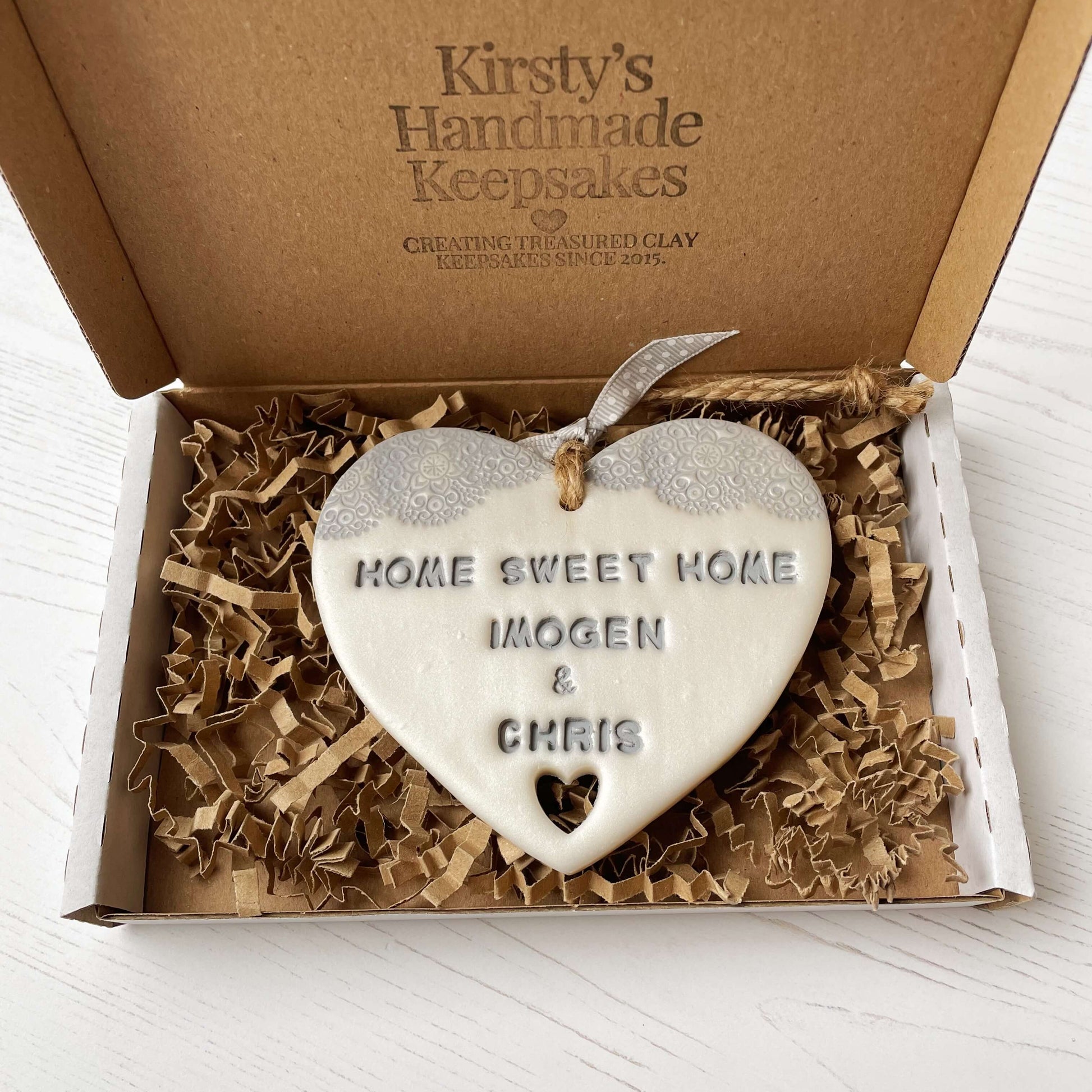 Personalised new home gift pearlised white clay heart with a grey lace edge at the top & a heart cut out at the bottom with twine for hanging personalised with HOME SWEET HOME IMOGEN & CHRIS