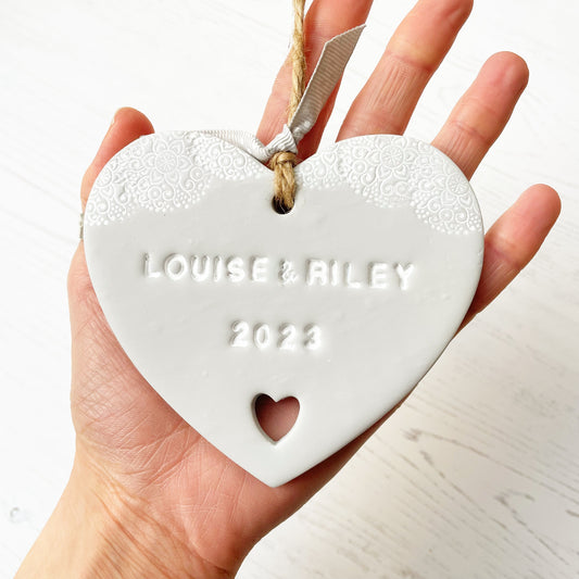 Personalised Valentine gift, grey clay heart with a white lace edge at the top of the heart and a heart cut out of the bottom with jute twine for hanging, the heart is personalised with LOUISE & RILEY 2023