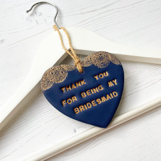 Personalised Bridesmaid thank you gift, navy clay hanging heart with a gold lace edge at the top of the heart, hanging off a white coat hanger, the heart is personalised with THANK YOU FOR BEING MY BRIDESMAID