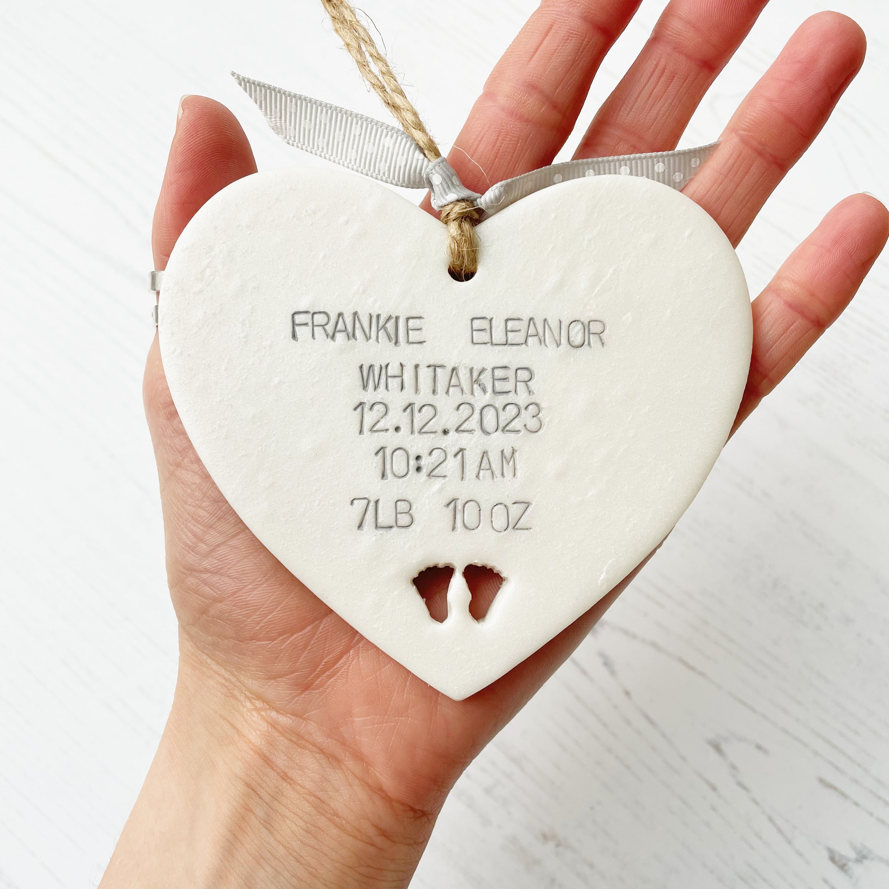 Personalised new baby keepsake heart gift in pearlised white personalised in grey with baby’s name, date, weight and time with two baby feet cut out at the bottom