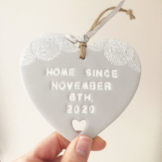 Personalised housewarming new home gift, grey clay heart with a white lace edge at the top of the heart and a heart cut out at the bottom with jute twine for hanging, the heart is personalised with HOME SINCE NOVEMBER 6TH, 2020