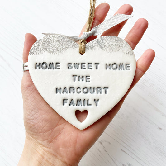 Personalised new home gift pearlised white clay heart with a grey lace edge at the top & a heart cut out at the bottom with twine for hanging personalised with HOME SWEET HOME THE HARCOURT FAMILY