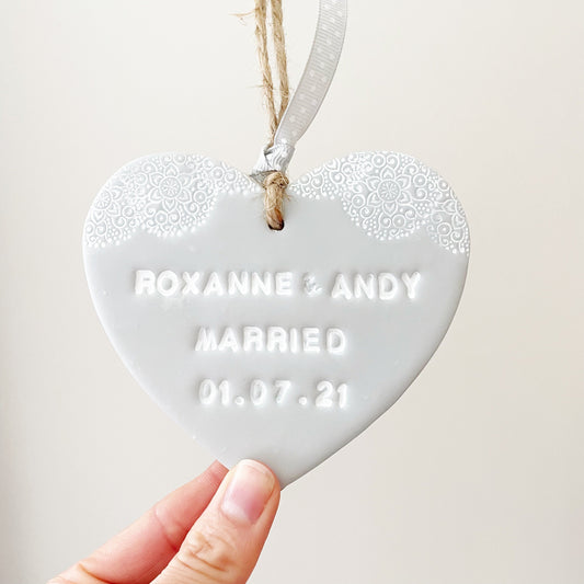Personalised wedding gift, grey clay heart with a white lace edge at the top of the heart with twine to hang, the heart is personalised with ROXANNE & ANDY MARRIED 01.07.21