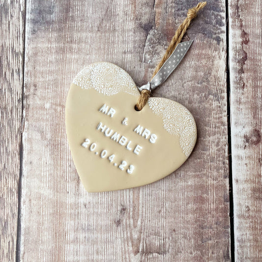 Personalised wedding gift, beige clay heart with a white lace edge at the top of the heart with twine to hang, the heart is personalised with MR & MRS HUMBLE 20.04.23
