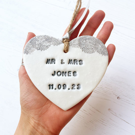 Personalised wedding gift, pearlised white clay hanging heart with a grey lace edge at the top of the heart, the heart is personalised with MR & MRS JONES 11.09.23