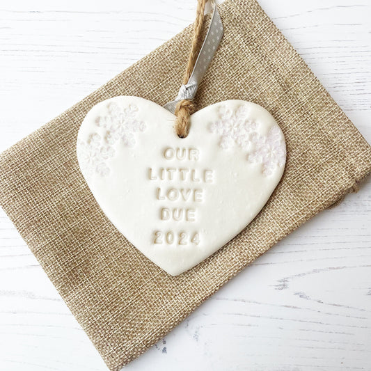 Personalised baby reveal Christmas heart ornament, pearlised white clay with OUR LITTLE LOVE DUE 2024 (text not painted), decorated with 2 iridescent glitter snowflakes on either side of the top of the heart