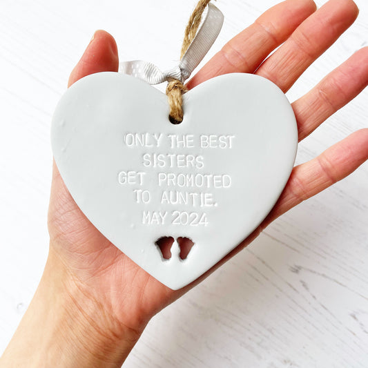 Grey clay hanging heart with baby feet cut out of the bottom, the heart is personalised with ONLY THE BEST SISTERS GET PROMOTED TO AUNTIE. MAY 2024