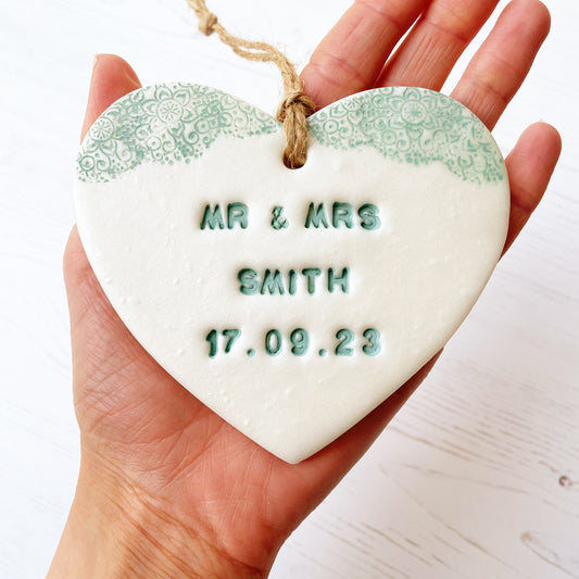 Personalised wedding gift, pearlised white clay hanging heart with a sage green lace edge at the top of the heart, the heart is personalised with MR & MRS SMITH 17.09.23