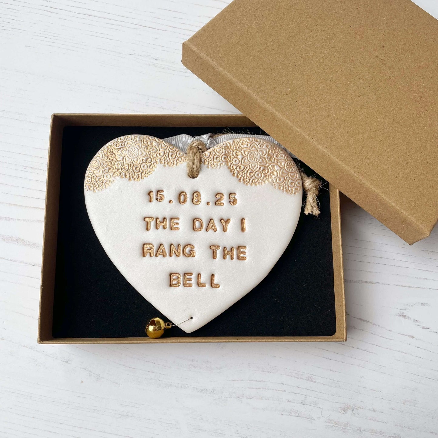 Personalised cancer survivor gift, pearlised white clay hanging heart with a gold lace edge at the top of the heart and a gold bell hanging below, the heart is personalised with 15.08.25 THE DAY I RANG THE BELL