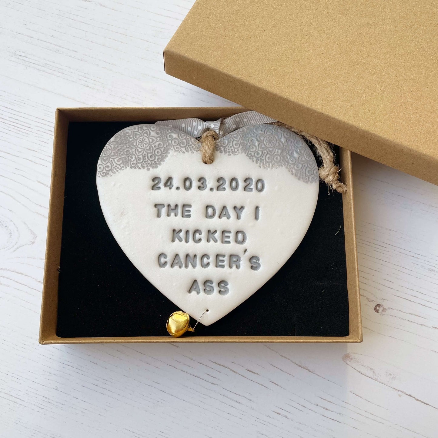 Personalised cancer survivor gift, pearlised white clay hanging heart with a grey lace edge at the top of the heart and a gold bell hanging below, the heart is personalised with 24.03.2020 THE DAY I KICKED CANCER’S ASS