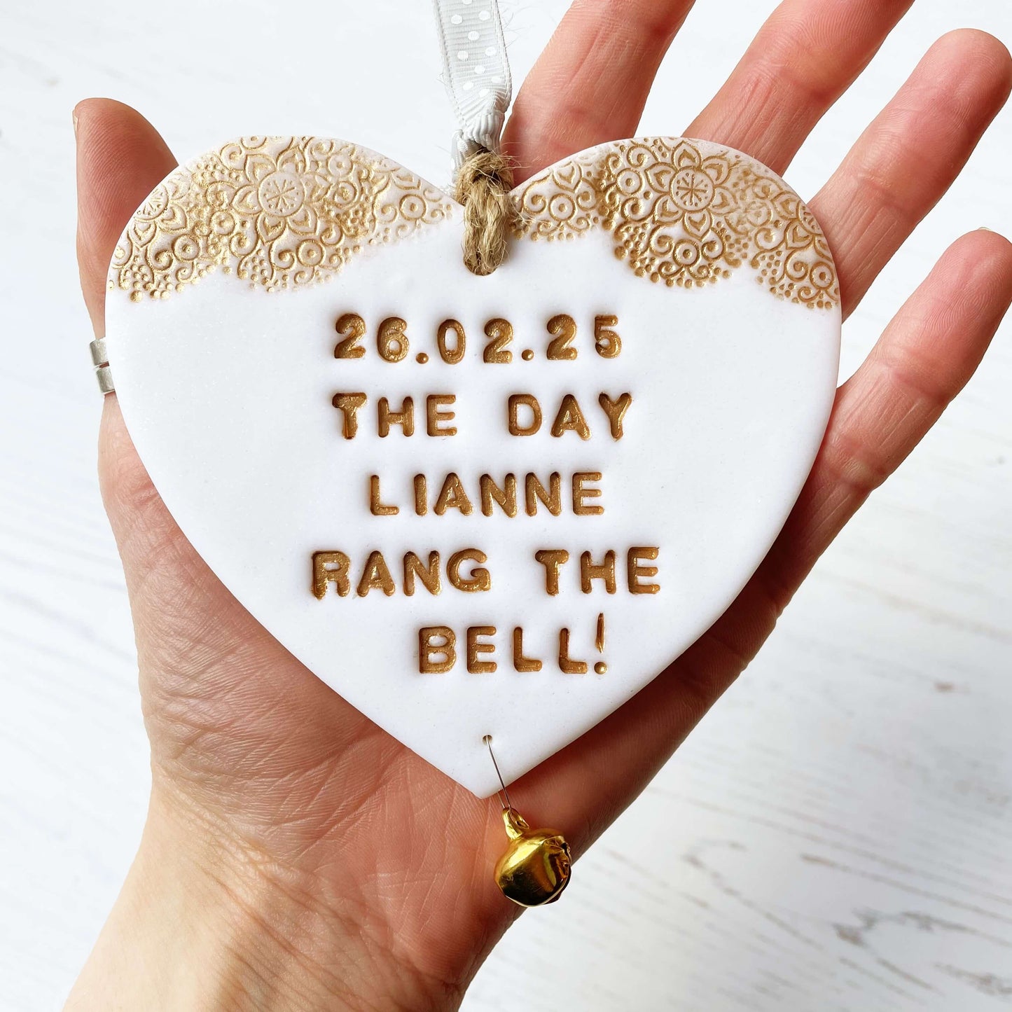 Personalised cancer survivor gift, glitter white clay hanging heart with a gold lace edge at the top of the heart and a gold bell hanging below, the heart is personalised with 26.02.25 THE DAY LIANNE RANG THE BELL!