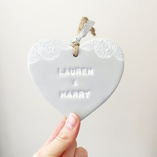 Personalised Valentine gift, grey clay heart with a white lace edge at the top of the heart with jute twine for hanging, the heart is personalised with LAUREN & HARRY