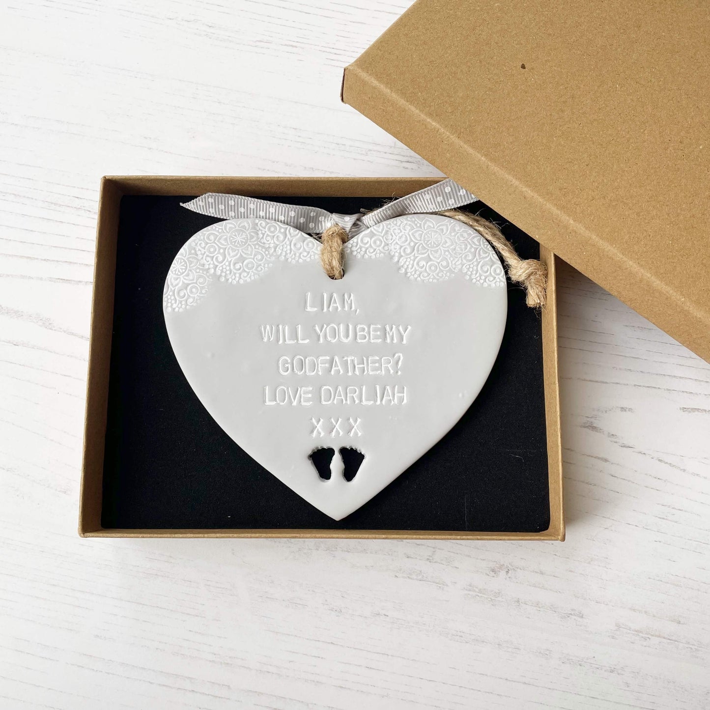 Personalised Godfather proposal gift, grey clay hanging heart with baby feet cut out of the bottom and white lace edge at the top of the heart, the heart is personalised with LIAM, WILL YOU BE MY GODFATHER? LOVE DARLIAH XXX