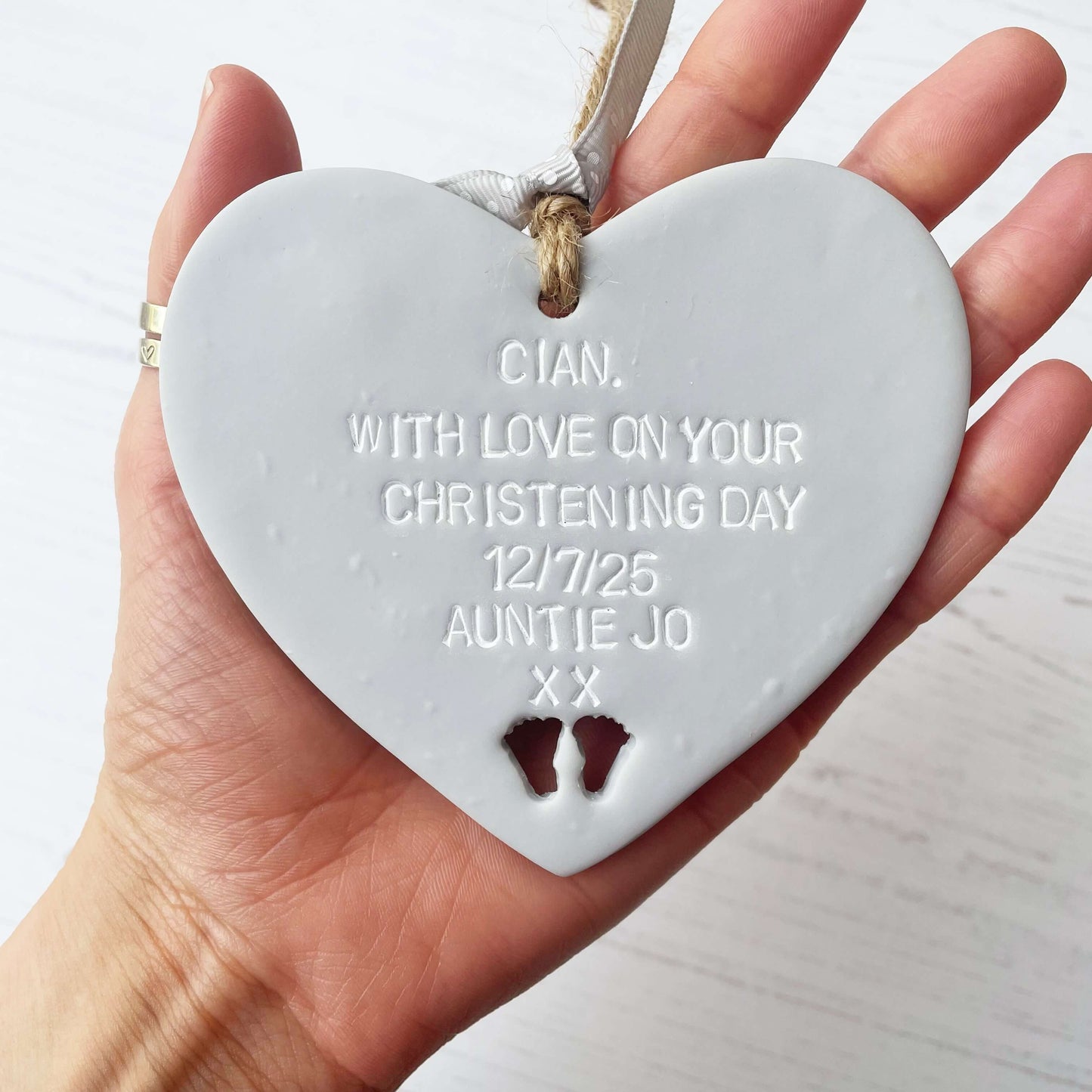 Personalised Christening baptism gift, grey clay hanging heart, with baby feet cut out of the bottom, the heart is personalised with CIAN, WITH LOVE ON YOUR CHRISTENING DAY 12/7/25 AUNTIE JO XX
