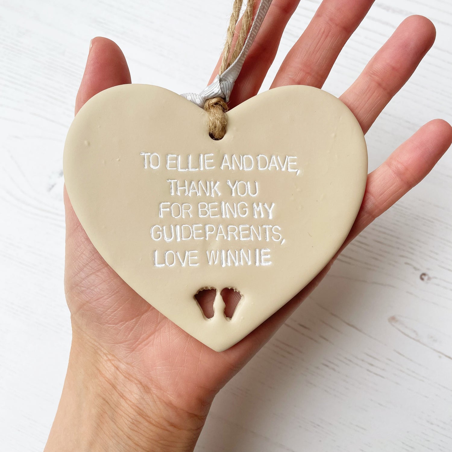 Personalised Guide parent gift, beige clay hanging heart with baby feet cut out of the bottom, the heart is personalised in white with TO ELLIE AND DAVE, THANK YOU FOR BEING MY GUIDEPARENTS, LOVE WINNIE