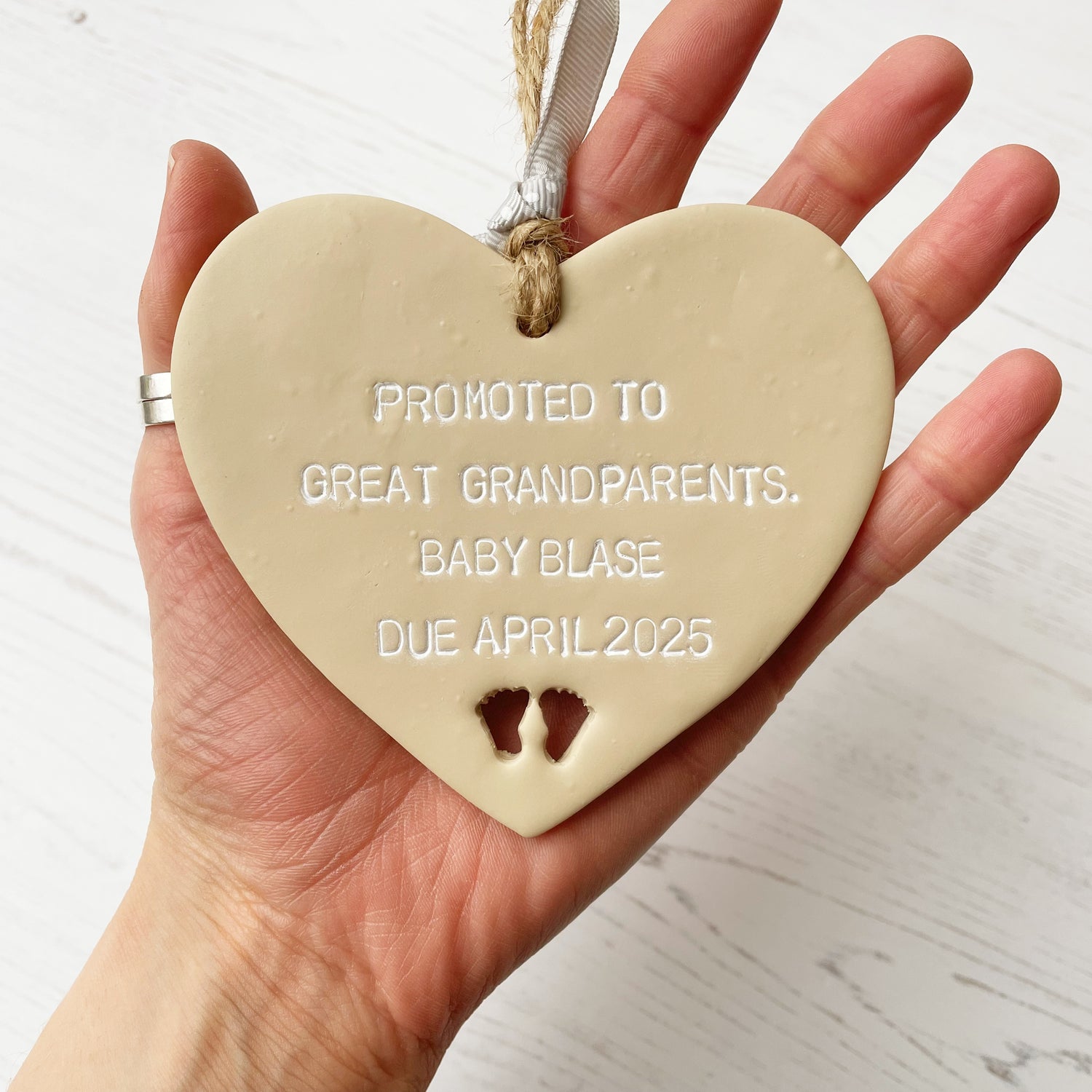 Beige clay hanging heart with baby feet cut out of the bottom and white personalisation, the heart is personalised with PROMOTED TO GREAT GRANDPARENTS. BABY BLASE DUE APRIL 2025