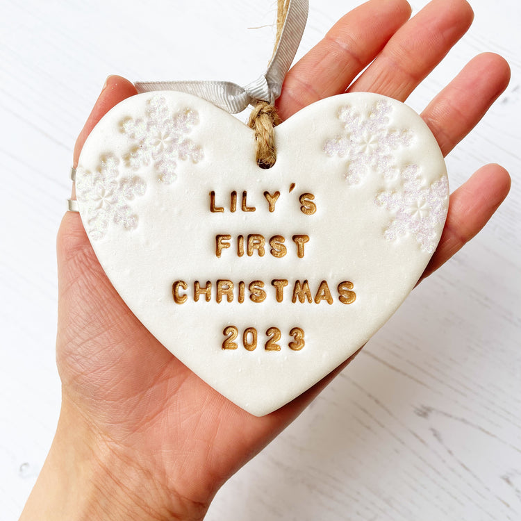 Personalised baby's first Christmas heart ornament, pearlised white clay with LILY'S FIRST CHRISTMAS 2023 painted gold, decorated with 2 iridescent glitter snowflakes on either side of the top of the heart