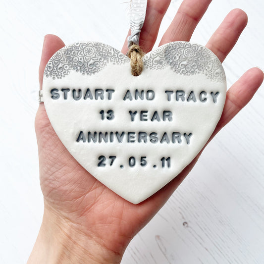 Personalised 13th anniversary gift, pearlised white clay hanging heart with a grey lace edge at the top of the heart, the heart is personalised with STUART AND TRACY 13 YEAR ANNIVERSARY 27.05.11