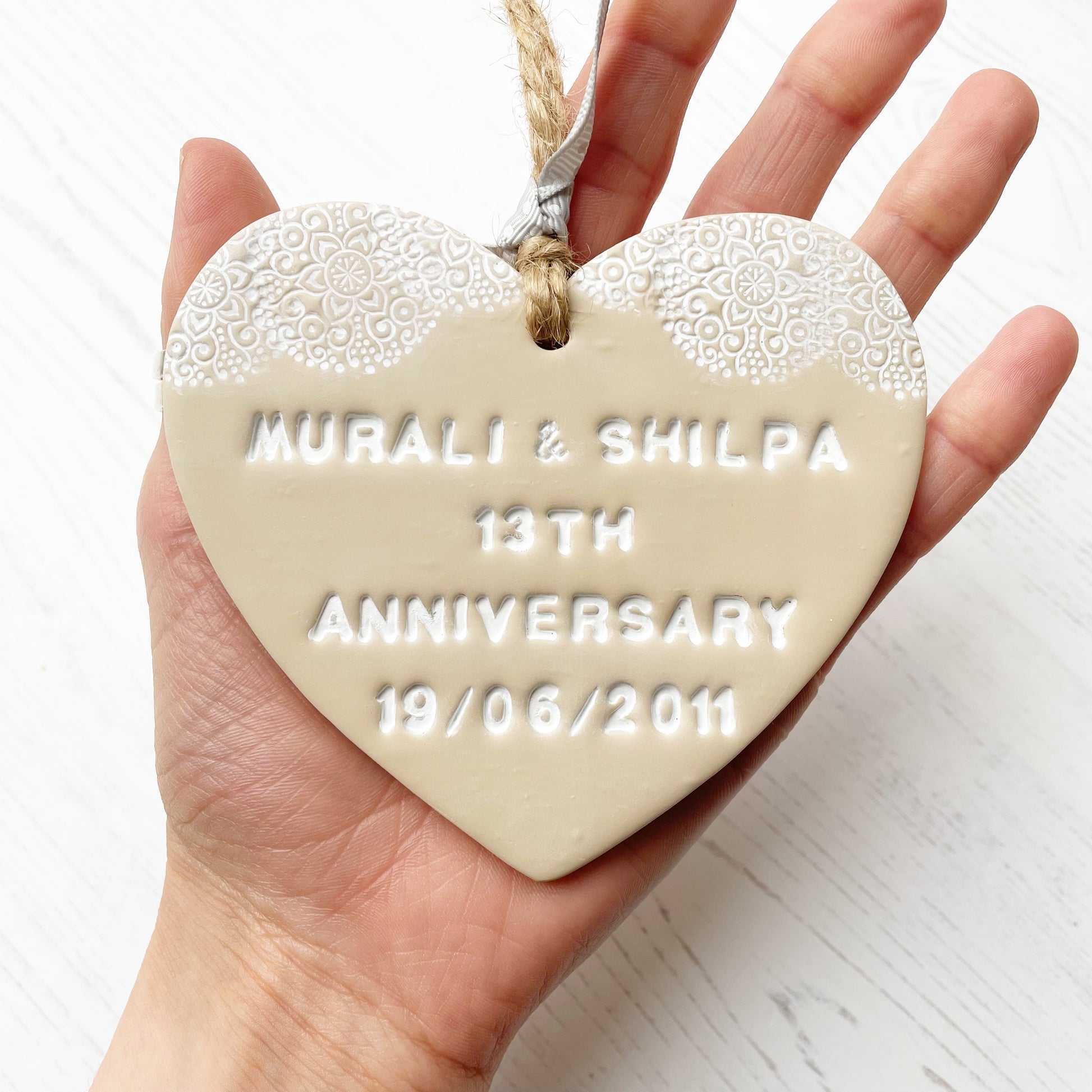 Personalised 13th anniversary gift, beige clay heart with a white lace edge at the top of the heart with jute twine for hanging, the heart is personalised with MURALI & SHILPA 13TH ANNIVERSARY 19/06/2011