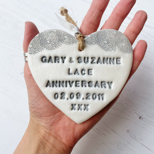 Personalised 13th anniversary gift, pearlised white clay hanging heart with a grey lace edge at the top of the heart, the heart is personalised with GARY & SUZANNE LACE ANNIVERSARY 02.09.2011 XXX