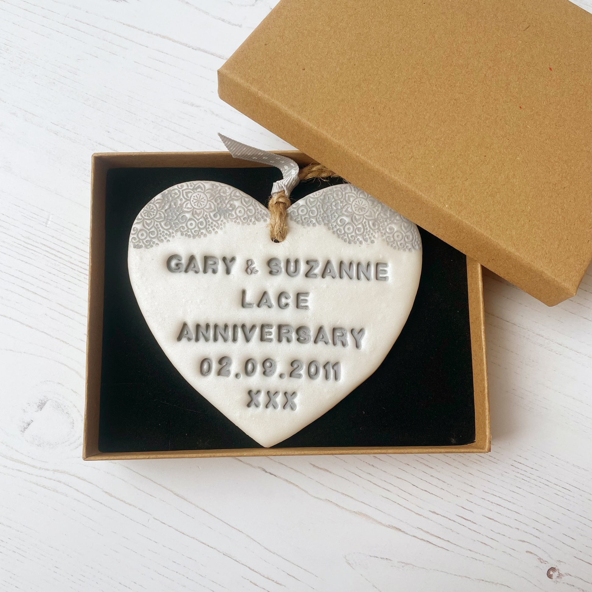 Personalised 13th anniversary gift, pearlised white clay hanging heart with a grey lace edge at the top of the heart, the heart is personalised with GARY & SUZANNE LACE ANNIVERSARY 02.09.2011 XXX