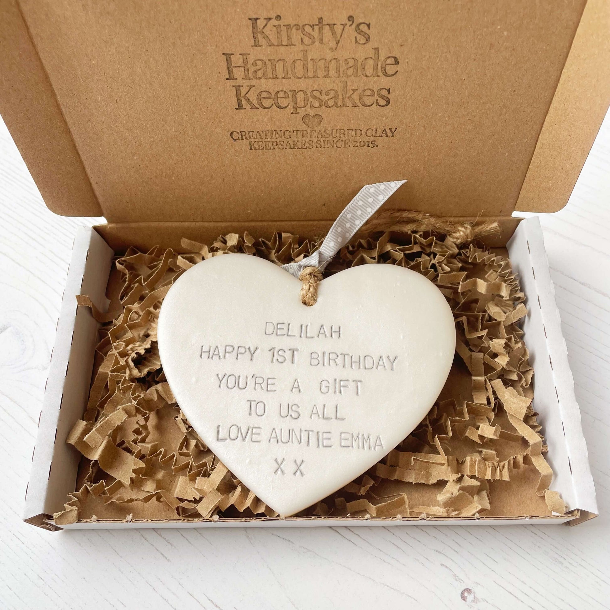 Personalised 1st birthday gift, pearlised white clay hanging heart, the heart is personalised in grey with DELILAH HAPPY 1ST BIRTHDAY YOU’RE A GIFT TO US ALL LOVE AUNTIE EMMA XX