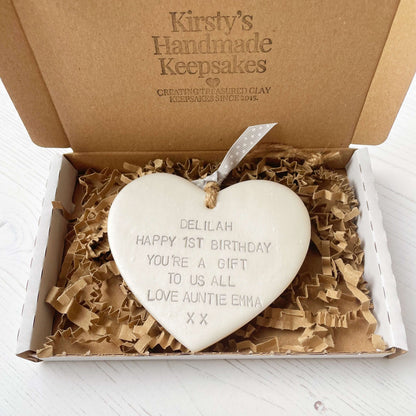 Personalised 1st birthday gift, pearlised white clay hanging heart, the heart is personalised in grey with DELILAH HAPPY 1ST BIRTHDAY YOU’RE A GIFT TO US ALL LOVE AUNTIE EMMA XX