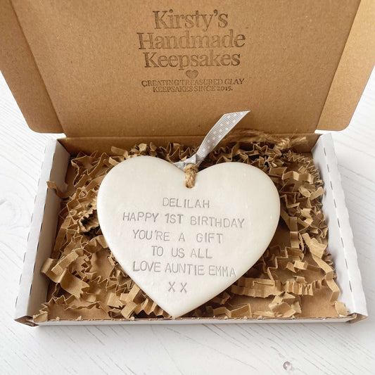 Personalised 1st birthday gift, pearlised white clay hanging heart, the heart is personalised in grey with DELILAH HAPPY 1ST BIRTHDAY YOU’RE A GIFT TO US ALL LOVE AUNTIE EMMA XX