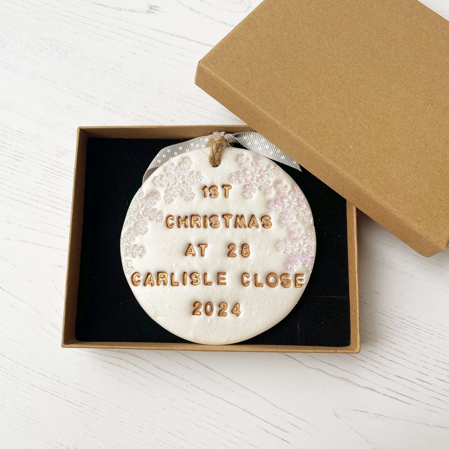 Personalised first Christmas in our new home bauble ornament, pearlised white round clay with 1ST CHRISTMAS AT 28 CARLISLE CLOSE 2024 in gold paint, decorated with 3 iridescent glitter snowflakes on either side of the bauble