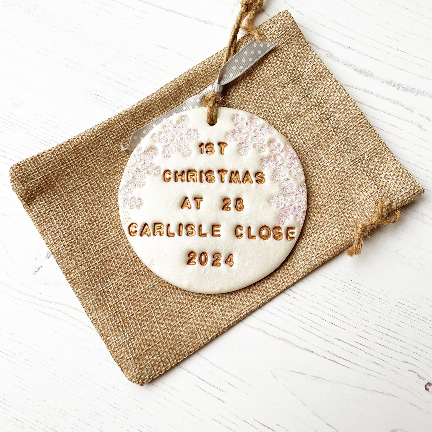 Personalised first Christmas in our new home bauble ornament, pearlised white round clay with 1ST CHRISTMAS AT 28 CARLISLE CLOSE 2024 in gold paint, decorated with 3 iridescent glitter snowflakes on either side of the bauble