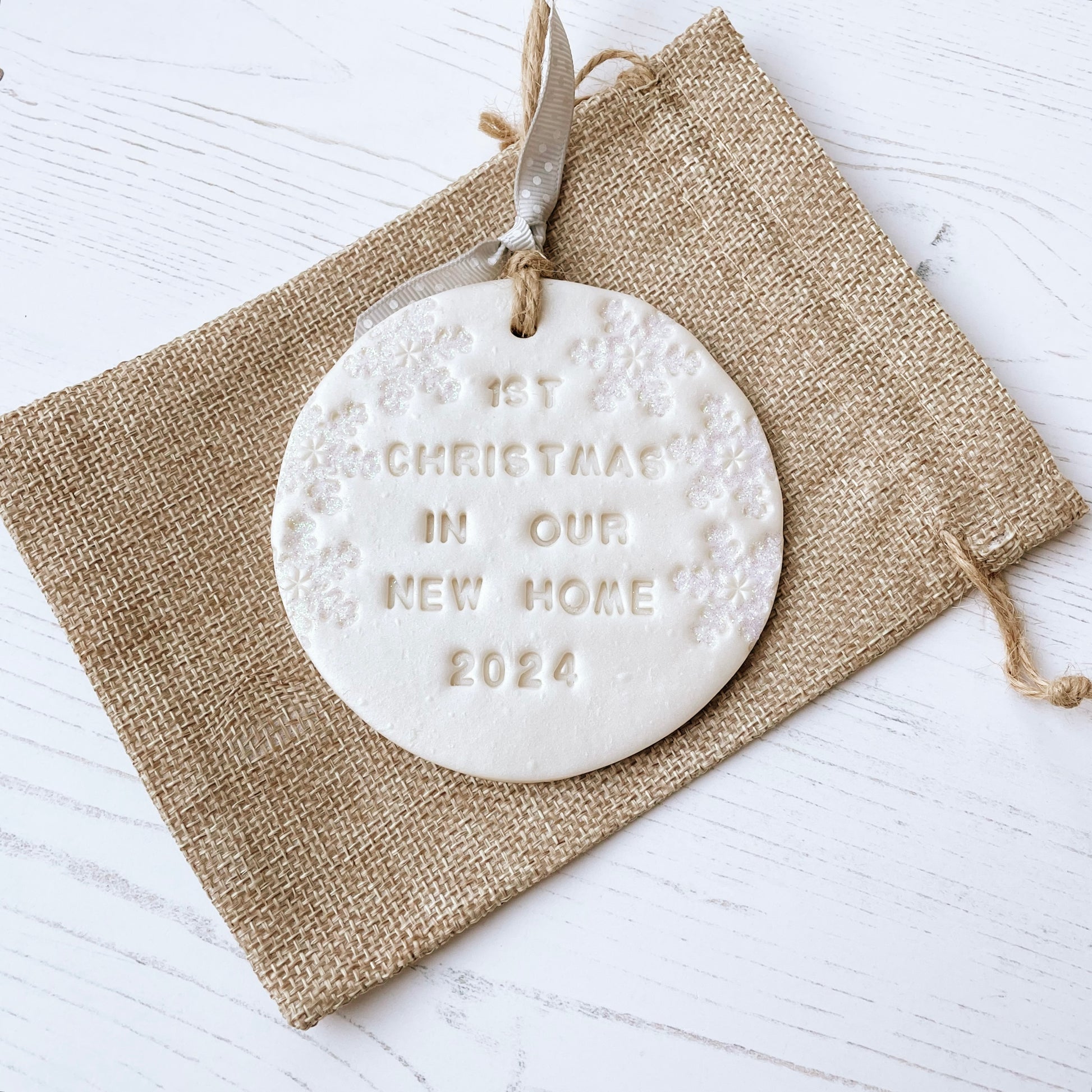 Personalised first Christmas in our new home bauble ornament, pearlised white round clay with 1ST CHRISTMAS IN OUR NEW HOME 2024 (text not painted), decorated with 3 iridescent glitter snowflakes on either side of the bauble