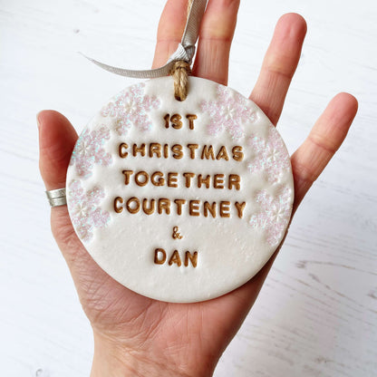 Personalised first Christmas together bauble ornament, pearlised white round clay with 1ST CHRISTMAS TOGETHER COURTENEY & DAN in gold paint, decorated with 3 iridescent glitter snowflakes on either side of the bauble
