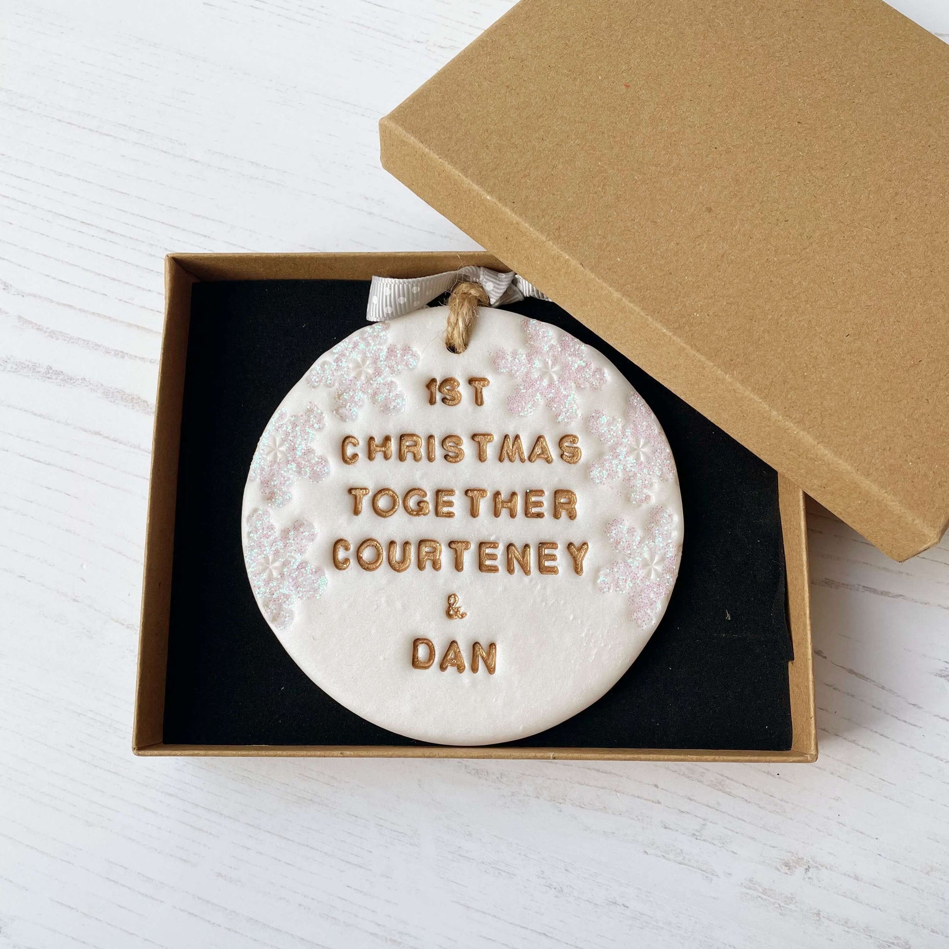 Personalised first Christmas together bauble ornament, pearlised white round clay with 1ST CHRISTMAS TOGETHER COURTENEY & DAN in gold paint, decorated with 3 iridescent glitter snowflakes on either side of the bauble
