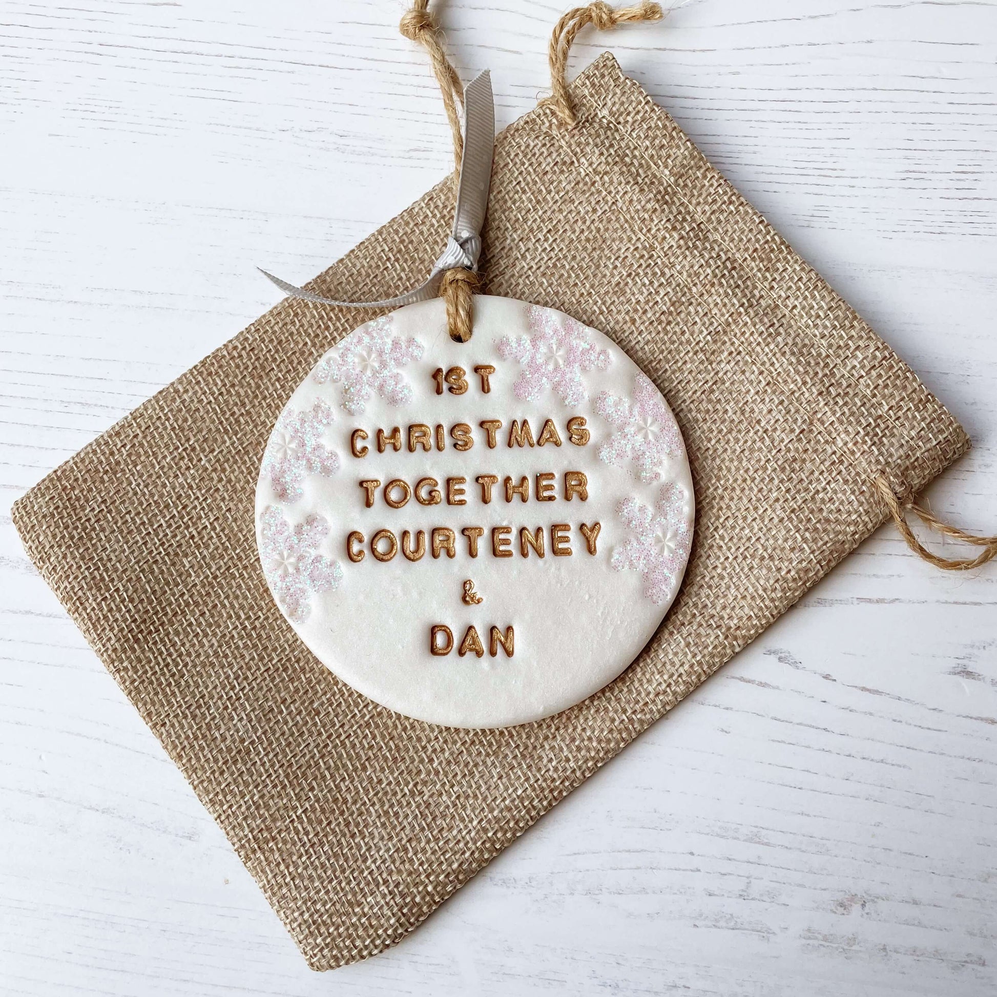 Personalised first Christmas together bauble ornament, pearlised white round clay with 1ST CHRISTMAS TOGETHER COURTENEY & DAN in gold paint, decorated with 3 iridescent glitter snowflakes on either side of the bauble