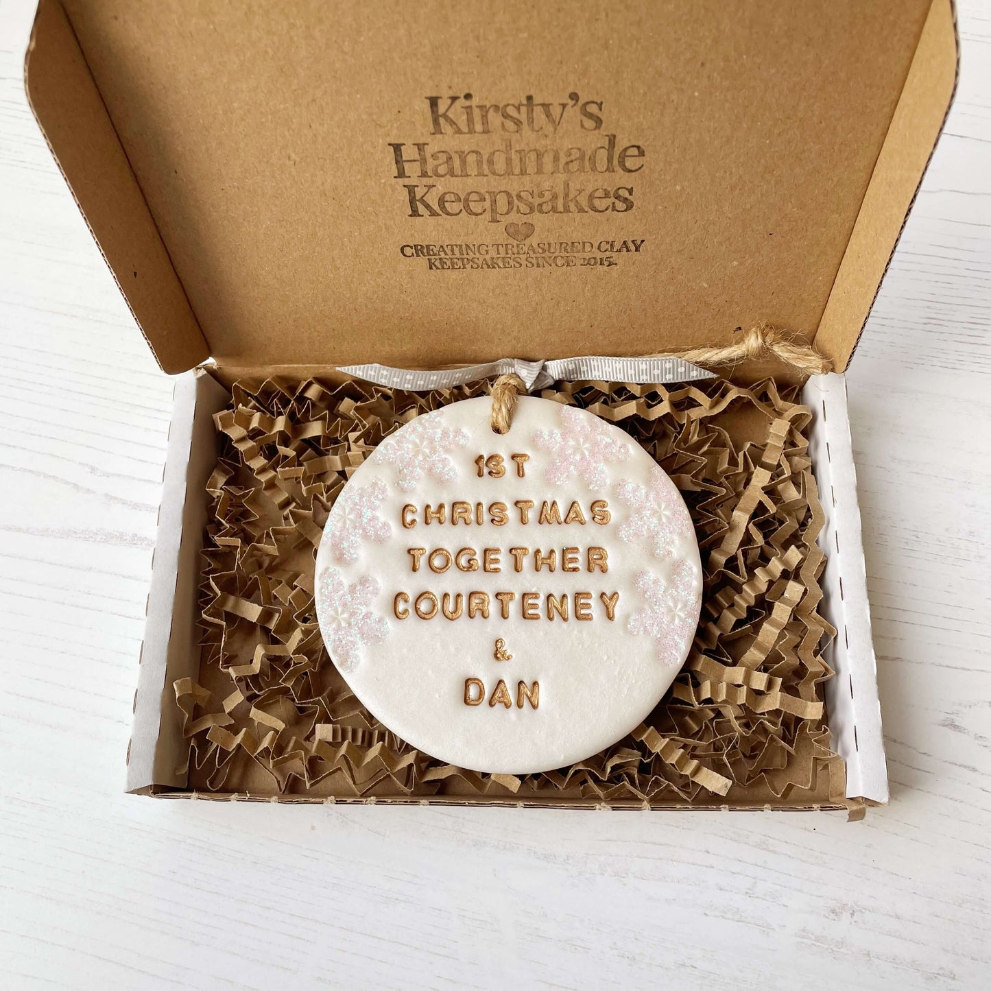 Personalised first Christmas together bauble ornament, pearlised white round clay with 1ST CHRISTMAS TOGETHER COURTENEY & DAN in gold paint, decorated with 3 iridescent glitter snowflakes on either side of the bauble