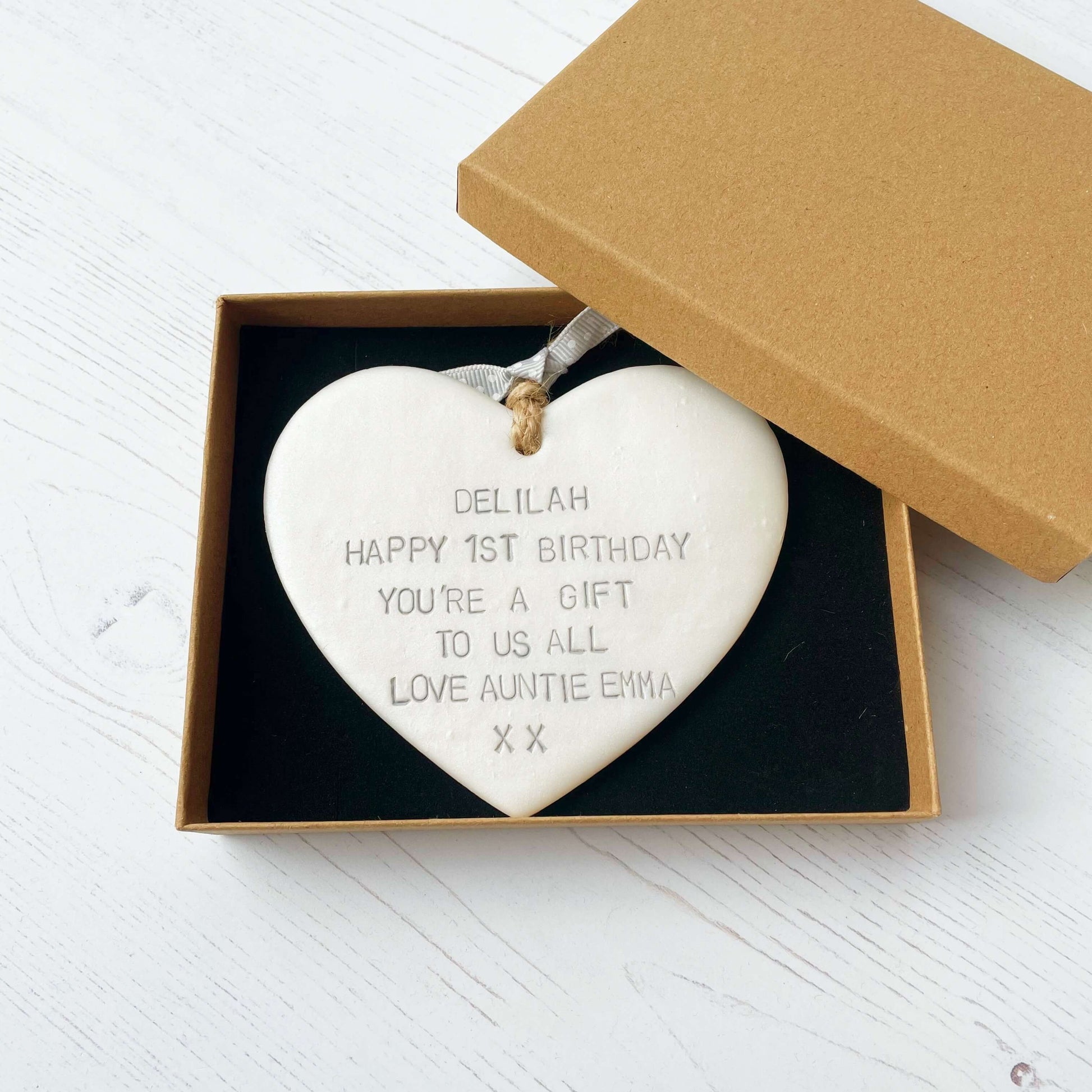 Personalised 1st birthday gift, pearlised white clay hanging heart, the heart is personalised in grey with DELILAH HAPPY 1ST BIRTHDAY YOU’RE A GIFT TO US ALL LOVE AUNTIE EMMA XX