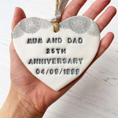 Personalised 25th anniversary gift, pearlised white clay hanging heart with a grey lace edge at the top of the heart, the heart is personalised with MUM AND DAD 25TH ANNIVERSARY 04/09/1999
