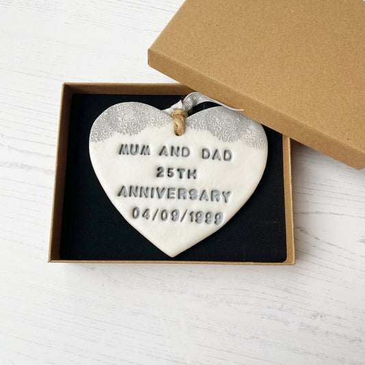 Personalised 25th anniversary gift, pearlised white clay hanging heart with a grey lace edge at the top of the heart, the heart is personalised with MUM AND DAD 25TH ANNIVERSARY 04/09/1999