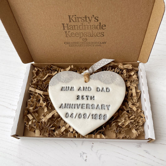 Personalised 25th anniversary gift, pearlised white clay hanging heart with a grey lace edge at the top of the heart, the heart is personalised with MUM AND DAD 25TH ANNIVERSARY 04/09/1999