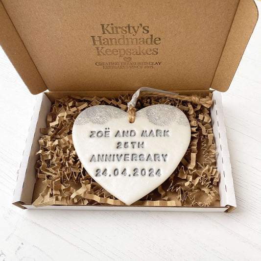Personalised 25th anniversary gift, pearlised white clay hanging heart with a grey lace edge at the top of the heart, the heart is personalised with ZOË AND MARK 25TH ANNIVERSARY 24.04.2024