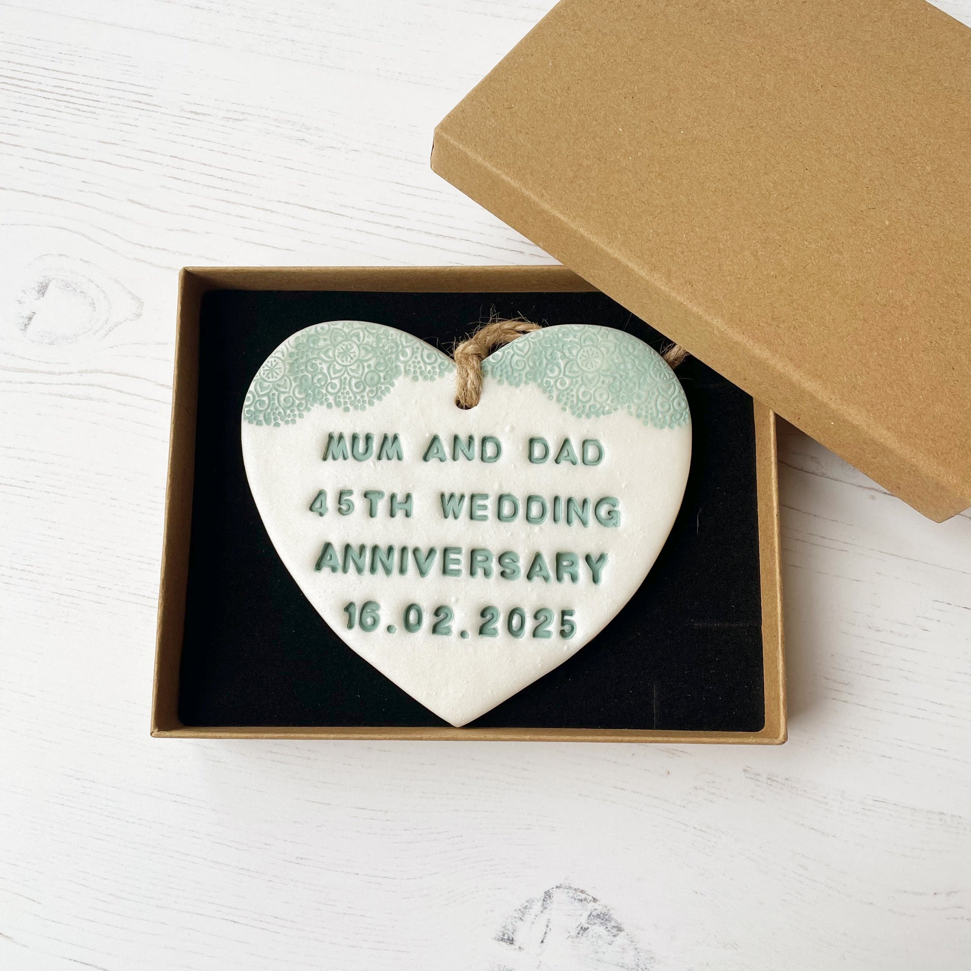 Personalised 13th anniversary gift, pearlised white clay hanging heart with a sage green lace edge at the top of the heart, the heart is personalised with MUM AND DAD 45TH WEDDING ANNIVERSARY 16.02.2025