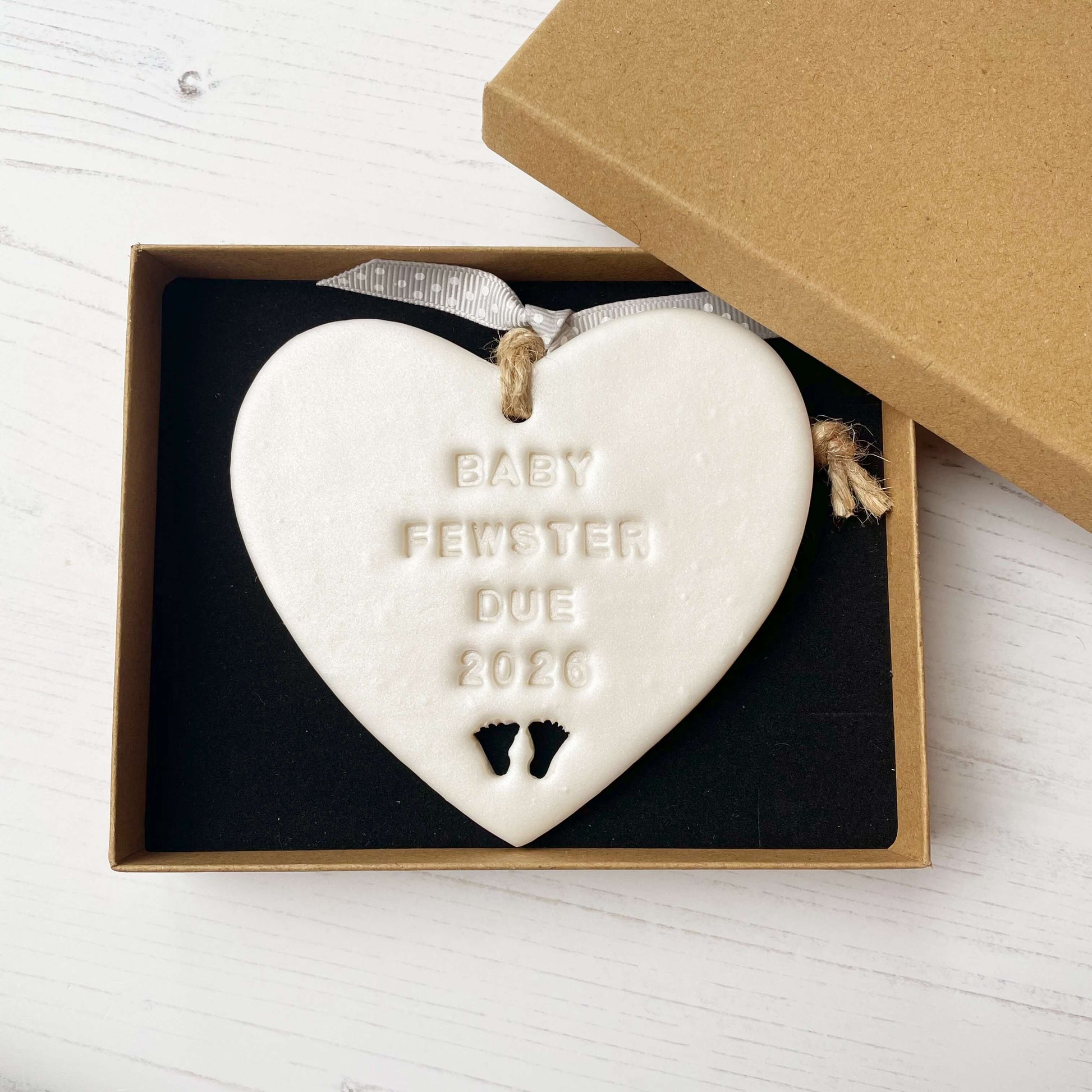 Personalised baby reveal gift, pearlised white clay heart with feet cut out of the bottom personalised with BABY FEWSTER DUE 2026