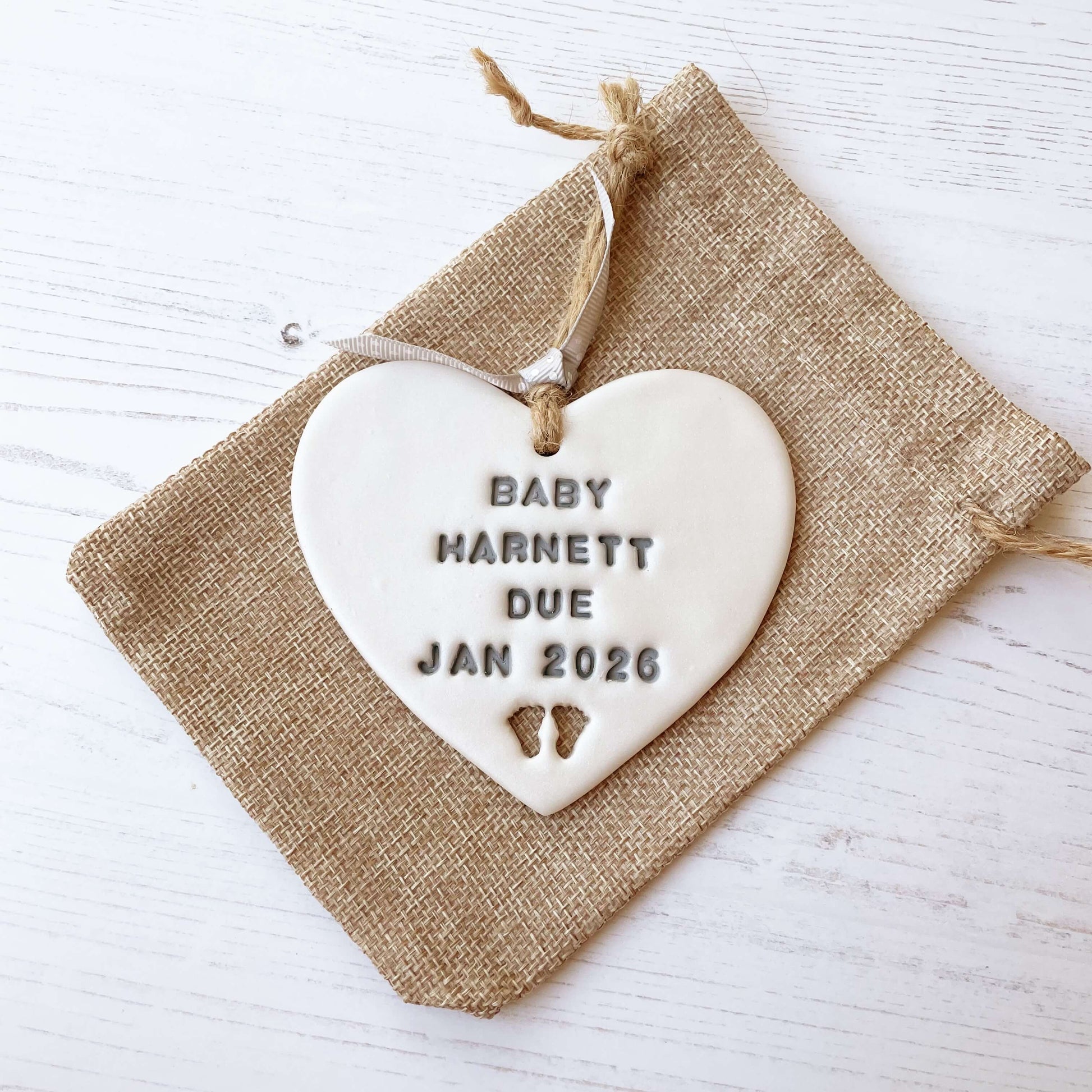 Personalised baby reveal gift, pearlised white clay heart with feet cut out of the bottom personalised in grey with BABY HARNETT DUE JAN 2026
