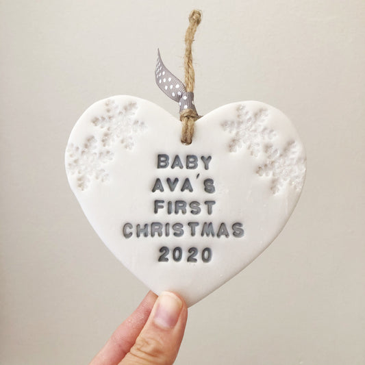 Personalised baby’s first Christmas heart ornament, pearlised white clay with BABY AVA’S FIRST CHRISTMAS 2020 painted grey, decorated with 2 iridescent glitter snowflakes on either side of the top of the heart