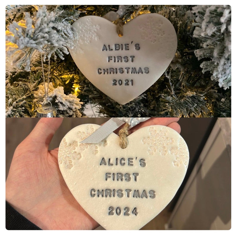 A split-screen photo showing two heart-shaped personalised Christmas ornaments hanging on a flocked Christmas tree and being held in a hand. The top ornament reads 'ALBIE'S FIRST CHRISTMAS 2021' and the bottom reads 'ALICE'S FIRST CHRISTMAS 2024'.