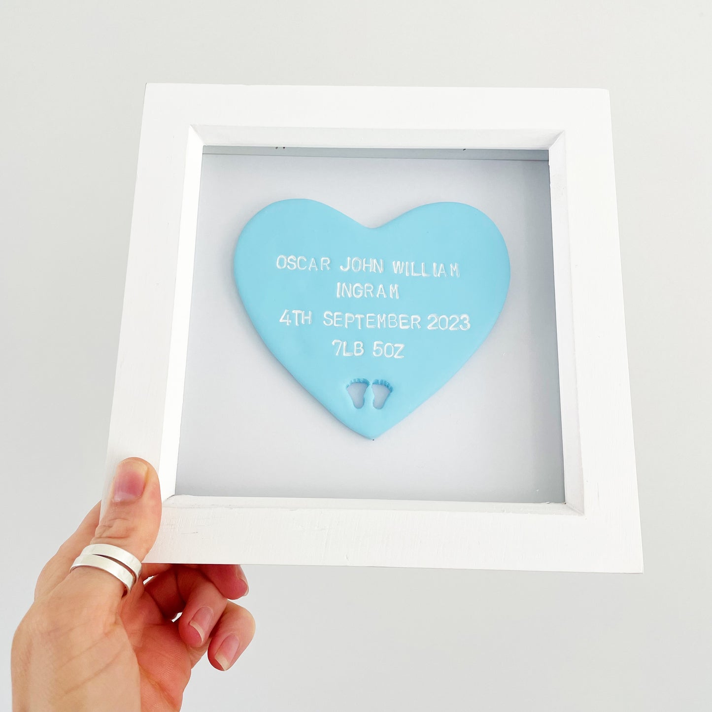 Personalised baby keepsake gift, pastel blue clay heart with baby feet cut out at the bottom of the heart in a white box frame, the heart is personalised with the baby’s name, date of birth, weight and time