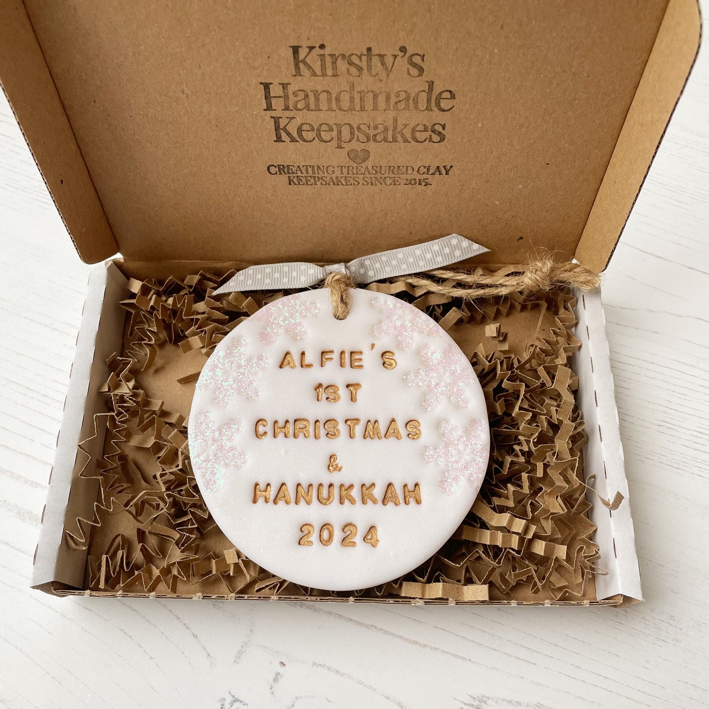 Personalised baby’s first Christmas and Hanukkah bauble ornament, glitter white clay round personalised with ALFIE’S FIRST CHRISTMAS & HANUKKAH 2024 in gold paint, decorated with 3 iridescent glitter snowflakes on either side of the bauble